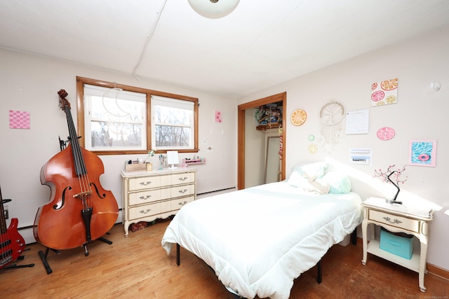 bedroom with baseboard heating, a closet, and hardwood / wood-style floors