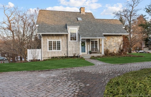 view of front of house featuring stone siding, a chimney, a front yard, and fence