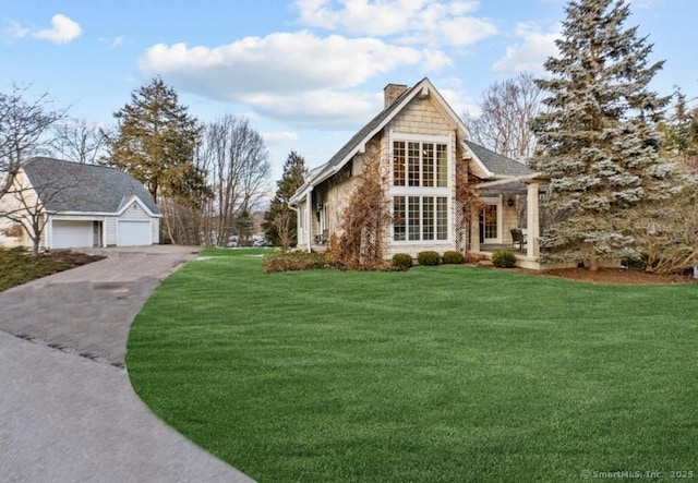 shingle-style home featuring a front yard, a detached garage, and a chimney