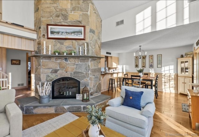 living area with visible vents, a towering ceiling, hardwood / wood-style flooring, an inviting chandelier, and a fireplace