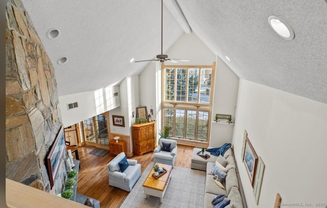 living area featuring visible vents, wood finished floors, a textured ceiling, a stone fireplace, and high vaulted ceiling