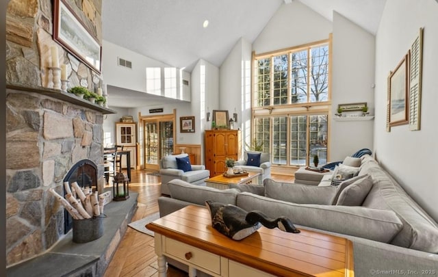 living area featuring light wood finished floors, high vaulted ceiling, a stone fireplace, and visible vents