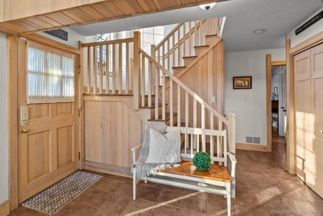 entryway featuring visible vents, stairway, wooden walls, a textured ceiling, and tile patterned flooring