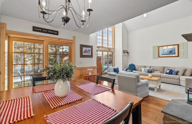 dining space featuring hardwood / wood-style flooring, a wainscoted wall, high vaulted ceiling, and a notable chandelier