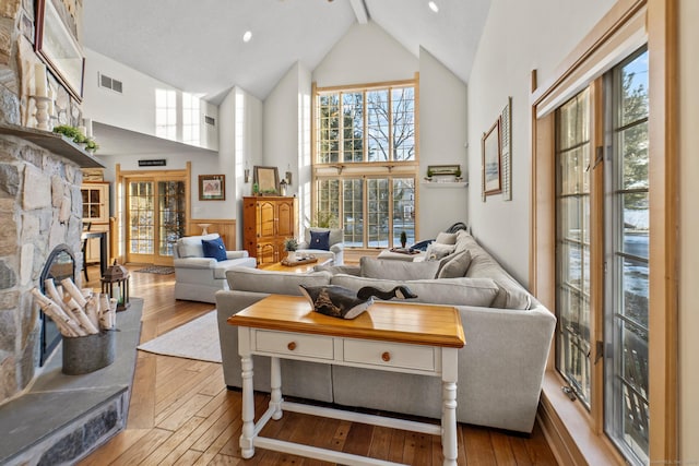 living area with visible vents, wainscoting, hardwood / wood-style flooring, a fireplace, and high vaulted ceiling