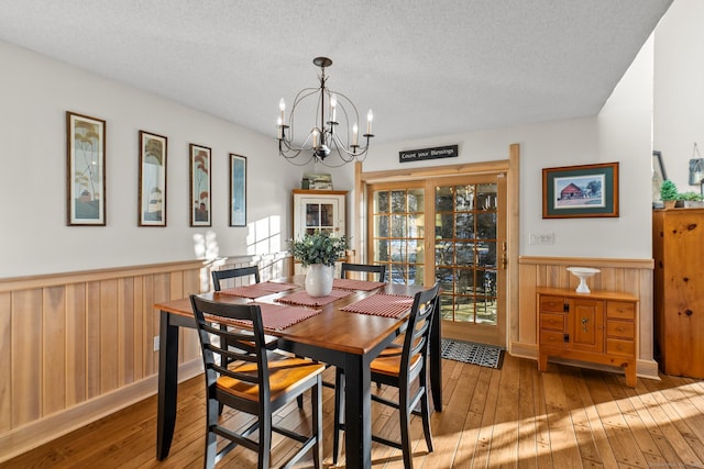 dining room featuring a wainscoted wall, a textured ceiling, a chandelier, and hardwood / wood-style floors