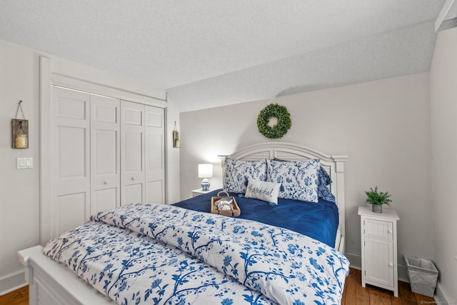 bedroom with a textured ceiling, lofted ceiling, wood finished floors, baseboards, and a closet