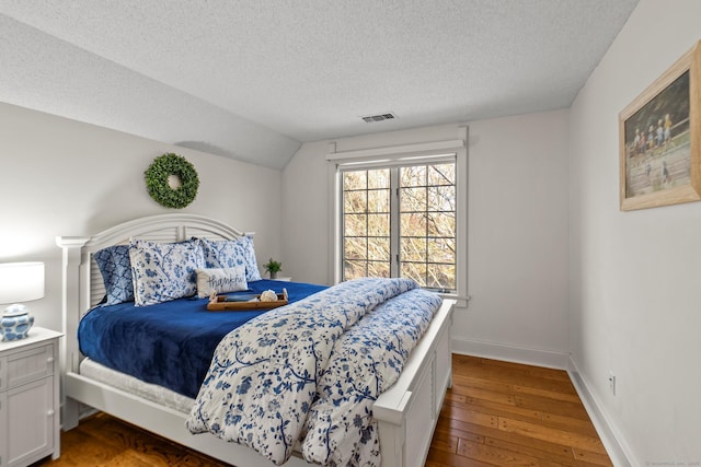 bedroom featuring visible vents, hardwood / wood-style floors, vaulted ceiling, a textured ceiling, and baseboards