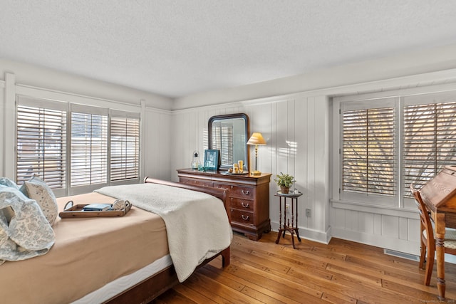 bedroom featuring hardwood / wood-style flooring, multiple windows, a decorative wall, and a textured ceiling