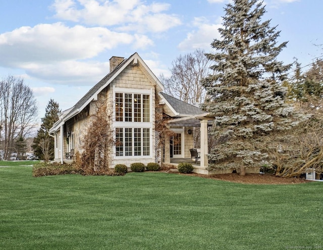 rear view of house with a shingled roof, a lawn, and a chimney