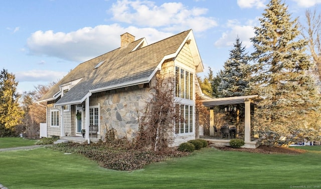 view of property exterior with a chimney, stone siding, a lawn, and a patio area