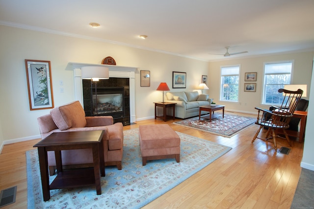 living room featuring crown molding, a fireplace, ceiling fan, and light hardwood / wood-style floors