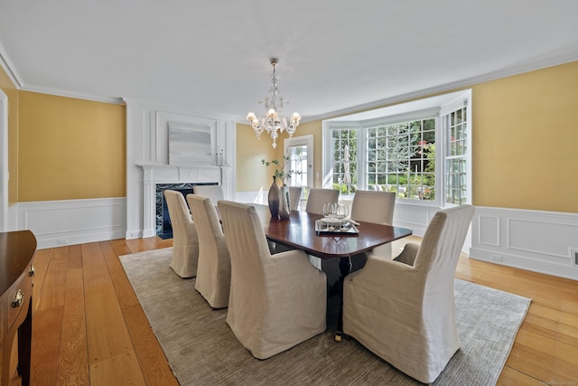 dining area with light wood-type flooring, crown molding, a high end fireplace, and an inviting chandelier