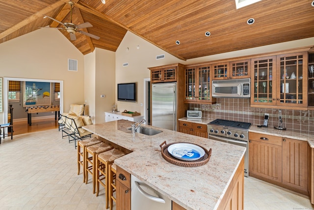 kitchen featuring light stone countertops, sink, high vaulted ceiling, high quality appliances, and an island with sink