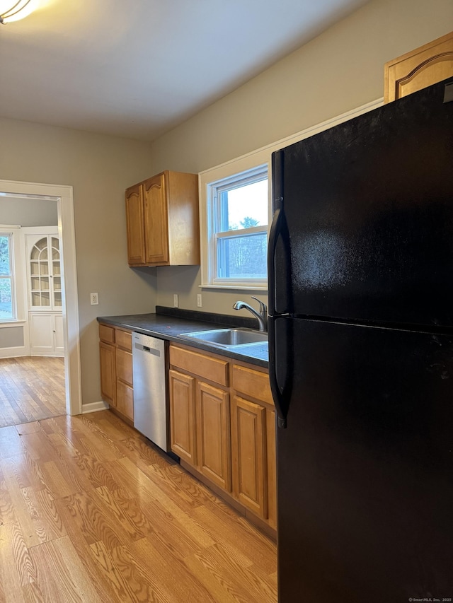 kitchen featuring black refrigerator, light hardwood / wood-style floors, stainless steel dishwasher, and sink