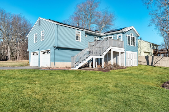 back of property featuring a lawn, a wooden deck, solar panels, and a garage