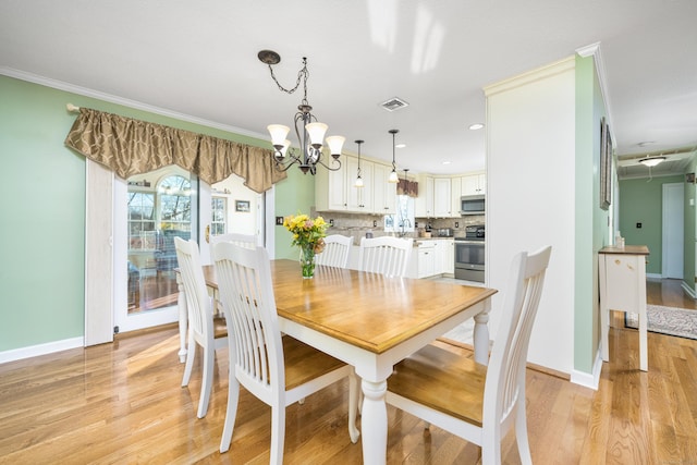 dining room with light hardwood / wood-style floors, sink, crown molding, and a chandelier