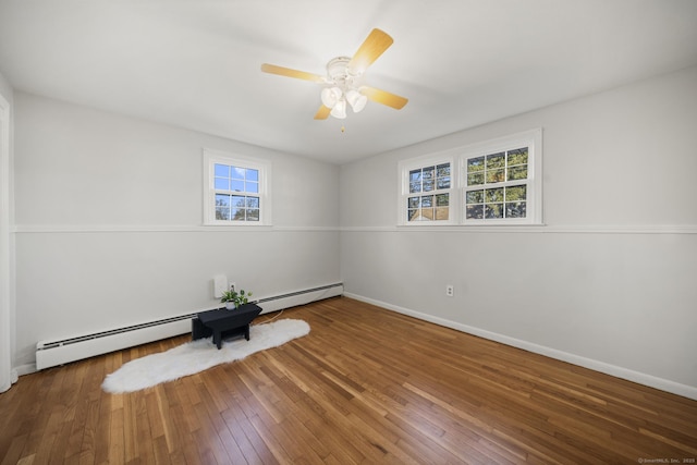 empty room with a baseboard heating unit, ceiling fan, hardwood / wood-style flooring, and a healthy amount of sunlight