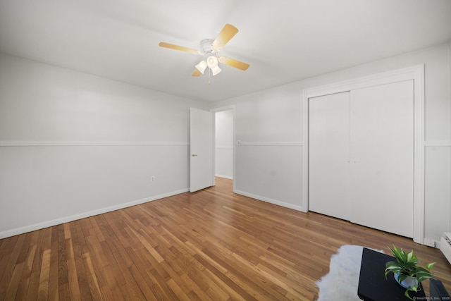 unfurnished bedroom featuring a baseboard radiator, hardwood / wood-style floors, a closet, and ceiling fan