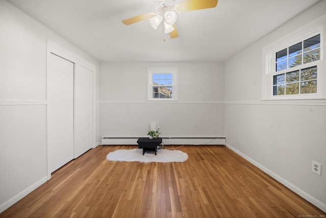 unfurnished bedroom featuring wood-type flooring, a baseboard radiator, ceiling fan, and multiple windows