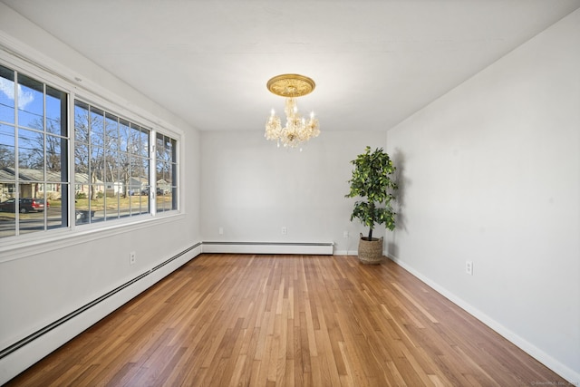 spare room featuring hardwood / wood-style floors, baseboard heating, and a notable chandelier