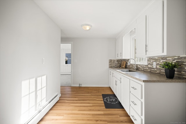 kitchen with white cabinets, baseboard heating, light hardwood / wood-style floors, and sink