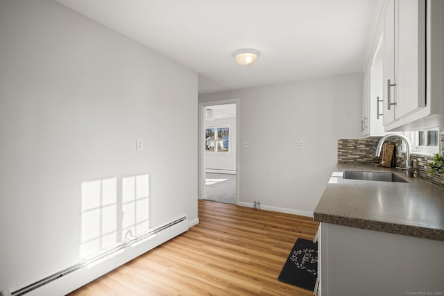 kitchen with sink, white cabinets, light wood-type flooring, backsplash, and baseboard heating