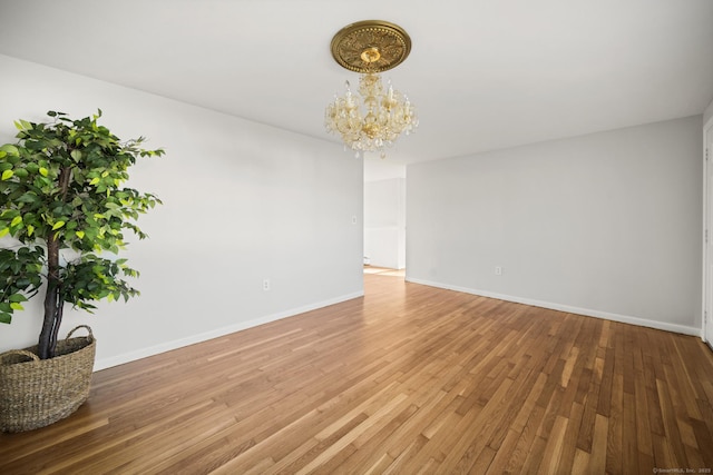 spare room with a chandelier and wood-type flooring