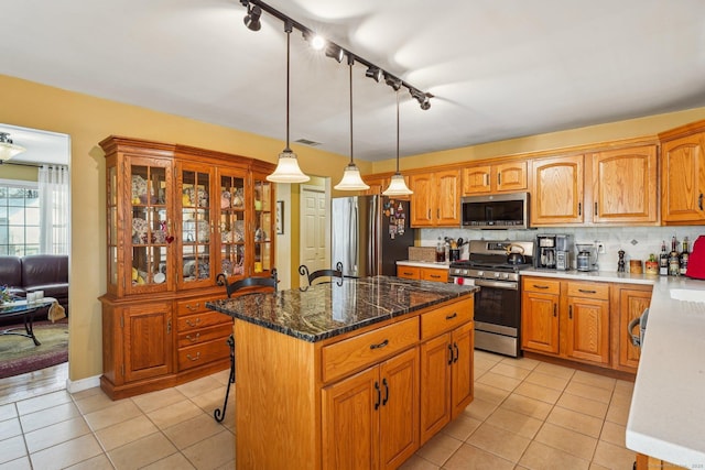 kitchen with pendant lighting, appliances with stainless steel finishes, a kitchen island, and light tile patterned floors