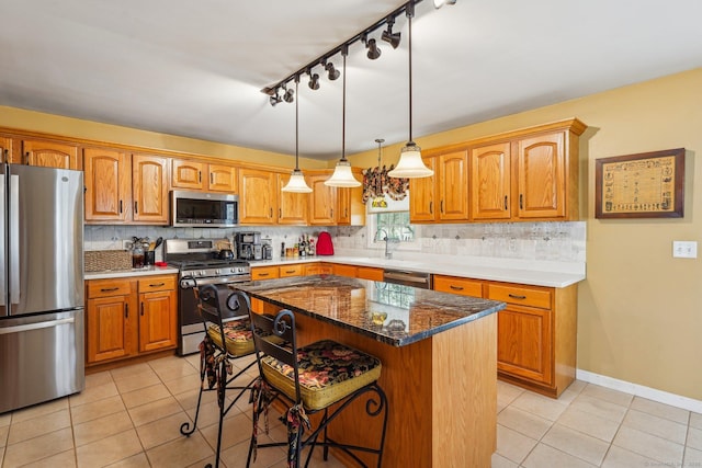 kitchen featuring light tile patterned floors, hanging light fixtures, stainless steel appliances, a center island, and dark stone counters