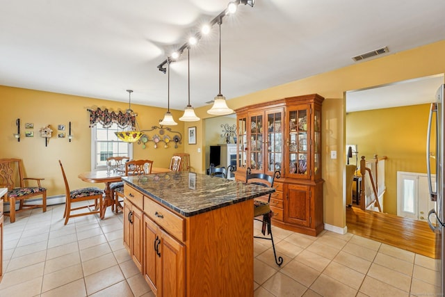 kitchen with pendant lighting, a kitchen bar, a kitchen island, light tile patterned flooring, and dark stone counters