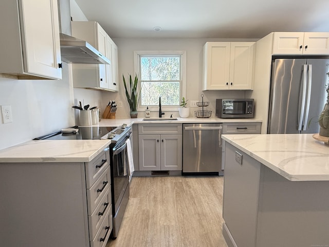 kitchen with white cabinetry, sink, light stone counters, stainless steel appliances, and wall chimney range hood