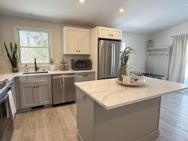 kitchen with sink, stainless steel appliances, a center island, light stone countertops, and white cabinets