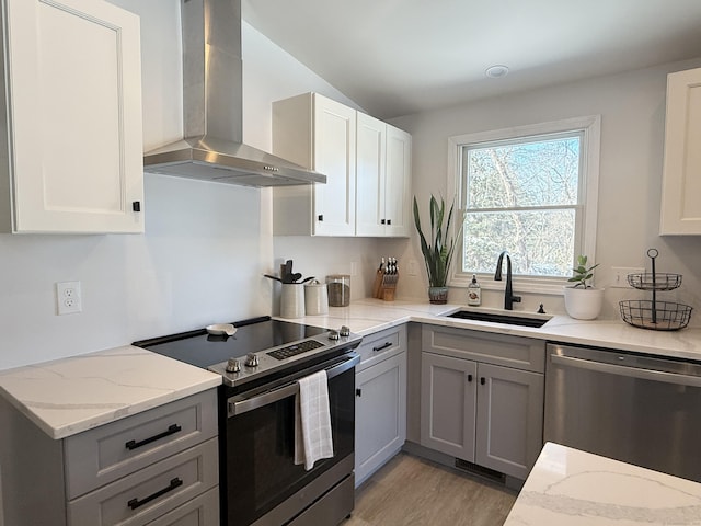 kitchen with sink, gray cabinetry, light stone counters, stainless steel appliances, and wall chimney range hood