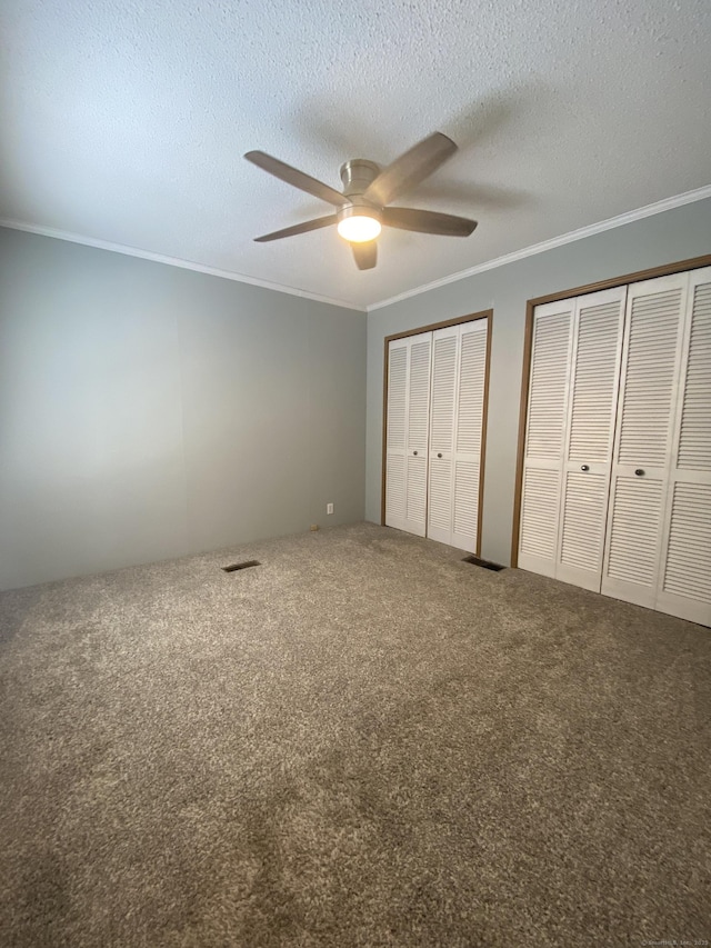 unfurnished bedroom featuring multiple closets, crown molding, carpet flooring, and ceiling fan