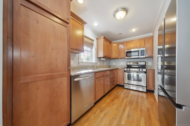 kitchen featuring stainless steel appliances, sink, crown molding, and light wood-type flooring