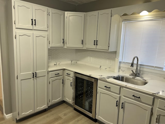 kitchen with backsplash, sink, light hardwood / wood-style flooring, white cabinets, and wine cooler