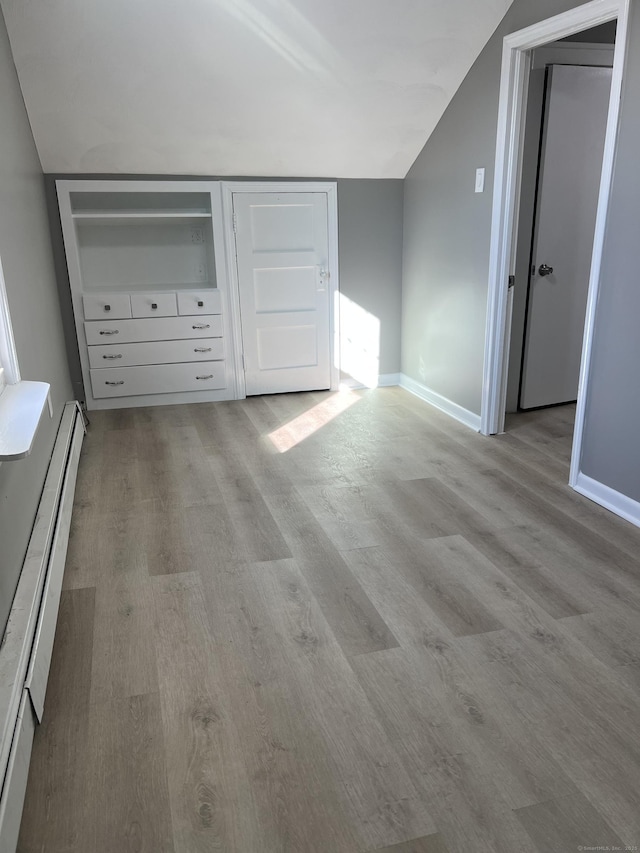 unfurnished bedroom featuring light hardwood / wood-style floors, lofted ceiling, and a baseboard heating unit