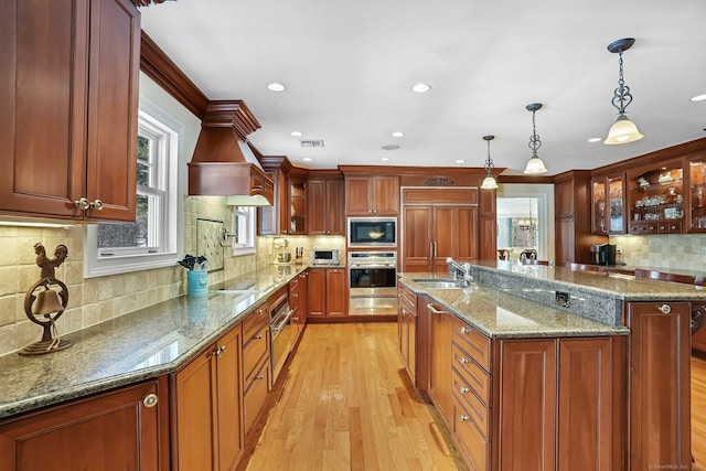 kitchen featuring built in appliances, a sink, light wood finished floors, glass insert cabinets, and pendant lighting