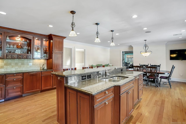 kitchen featuring light wood finished floors, crown molding, pendant lighting, and a sink