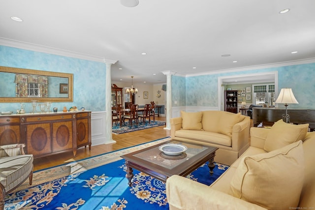 living area featuring wallpapered walls, a wainscoted wall, ornamental molding, wood finished floors, and ornate columns