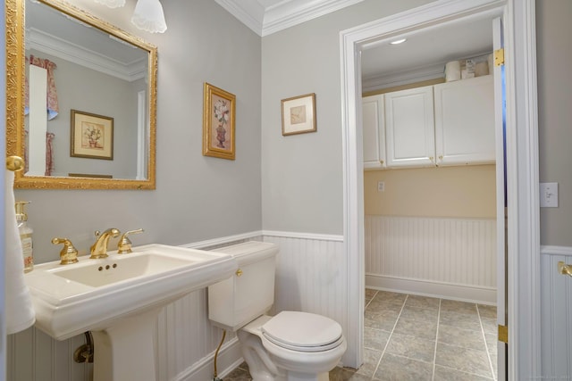 bathroom featuring toilet, a wainscoted wall, ornamental molding, tile patterned flooring, and a sink