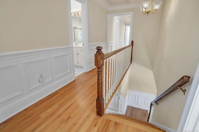 corridor featuring a wainscoted wall, crown molding, an inviting chandelier, light wood-style floors, and an upstairs landing