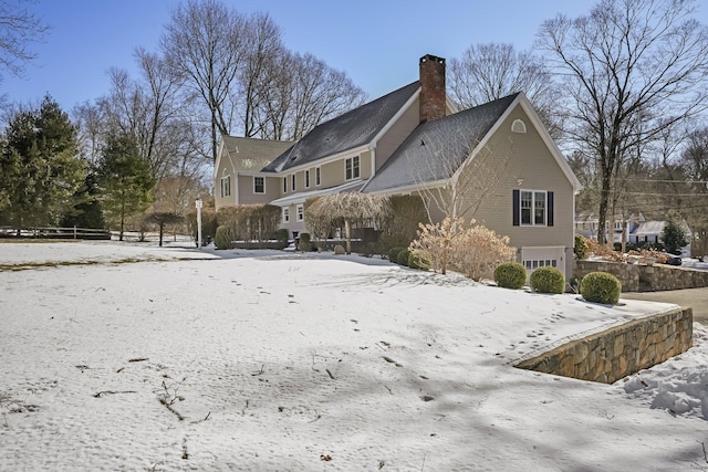 snow covered property with a garage and a chimney