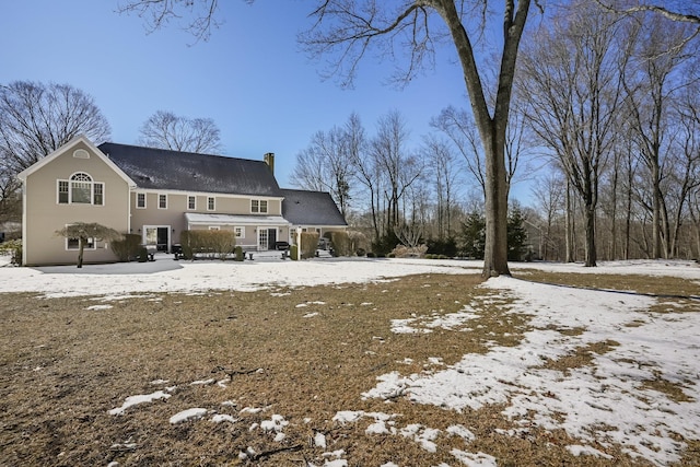 snow covered rear of property with a chimney