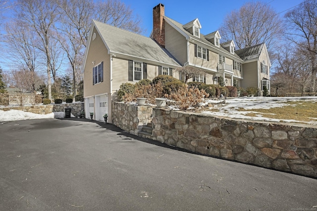 view of side of property with driveway, a chimney, and an attached garage