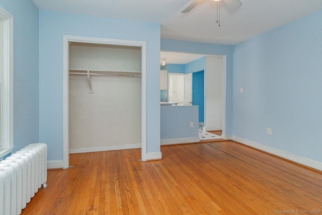 unfurnished bedroom featuring radiator, light hardwood / wood-style floors, a closet, and ceiling fan