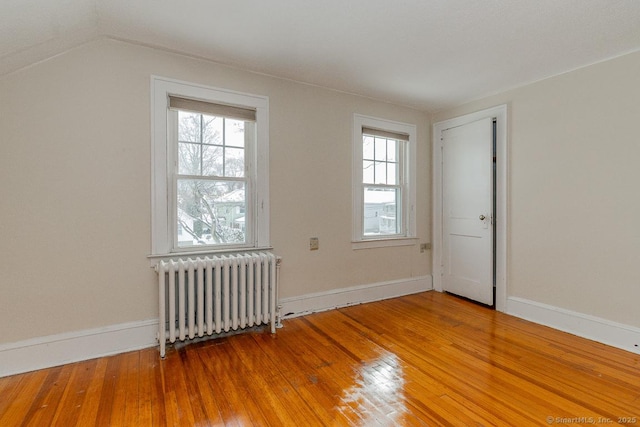 empty room with vaulted ceiling, radiator heating unit, hardwood / wood-style floors, and plenty of natural light