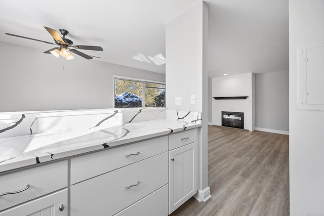 kitchen featuring a fireplace, white cabinets, ceiling fan, light hardwood / wood-style floors, and light stone countertops