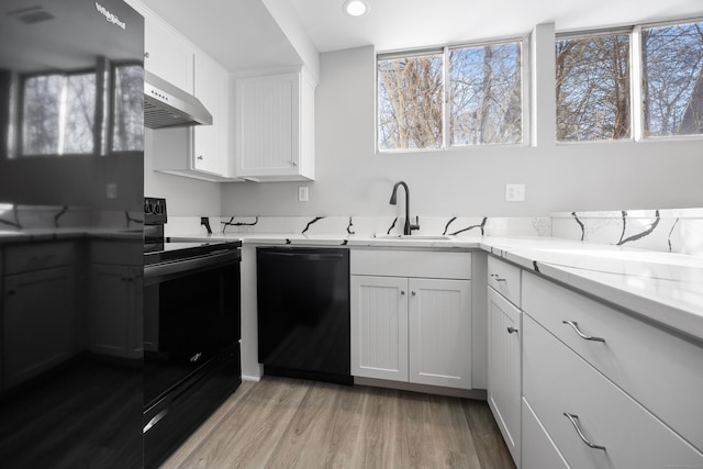 kitchen with white cabinetry, light stone counters, light hardwood / wood-style flooring, range hood, and black appliances